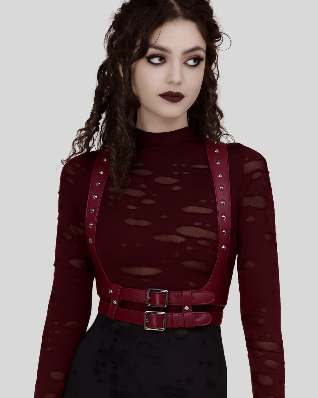 model wearing burgundy leather body harness with silver studs over distressed burgundy top