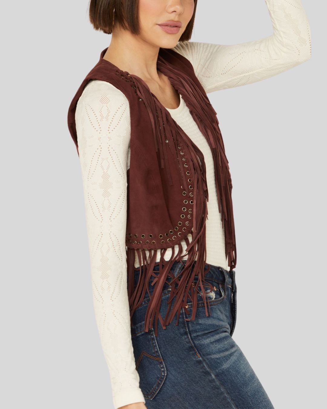  Woman wearing a burgundy suede fringe vest with grommet detailing, front view.
