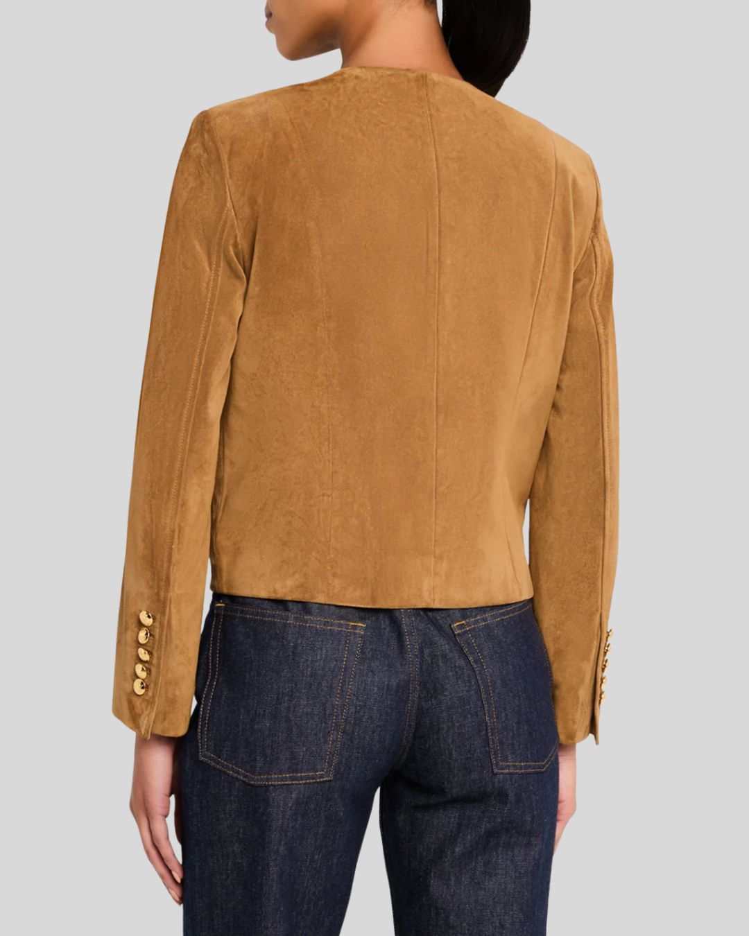 Full body view of woman wearing suede jacket with gold buttons and jeans