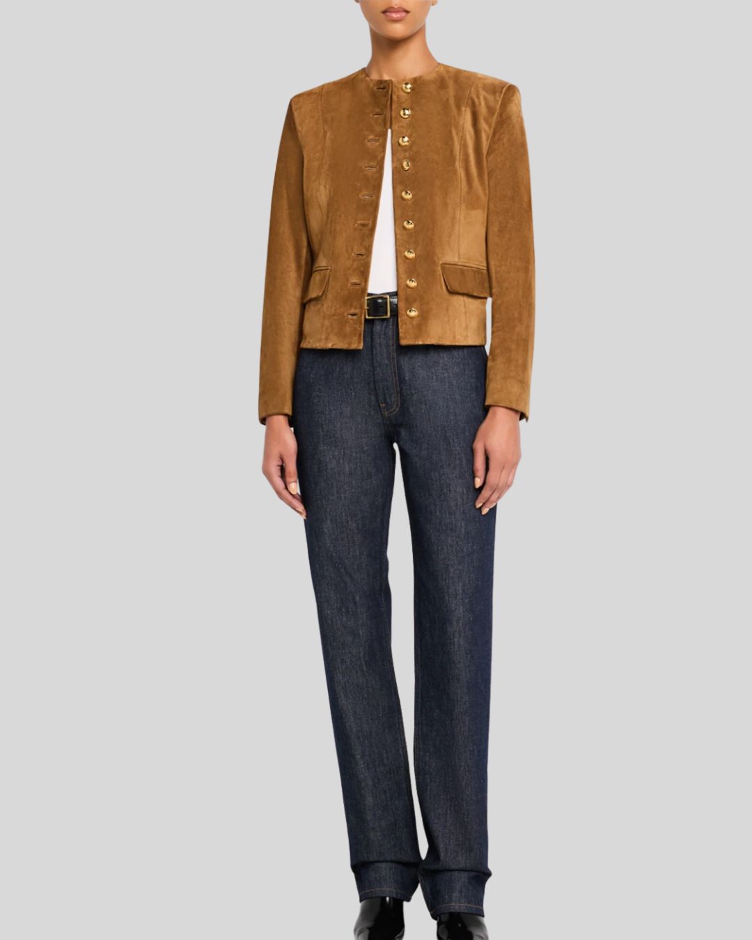 Full body view of woman wearing suede jacket with gold buttons and jeans
