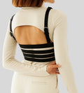 Woman wearing black leather body harness over cream outfit, rear view