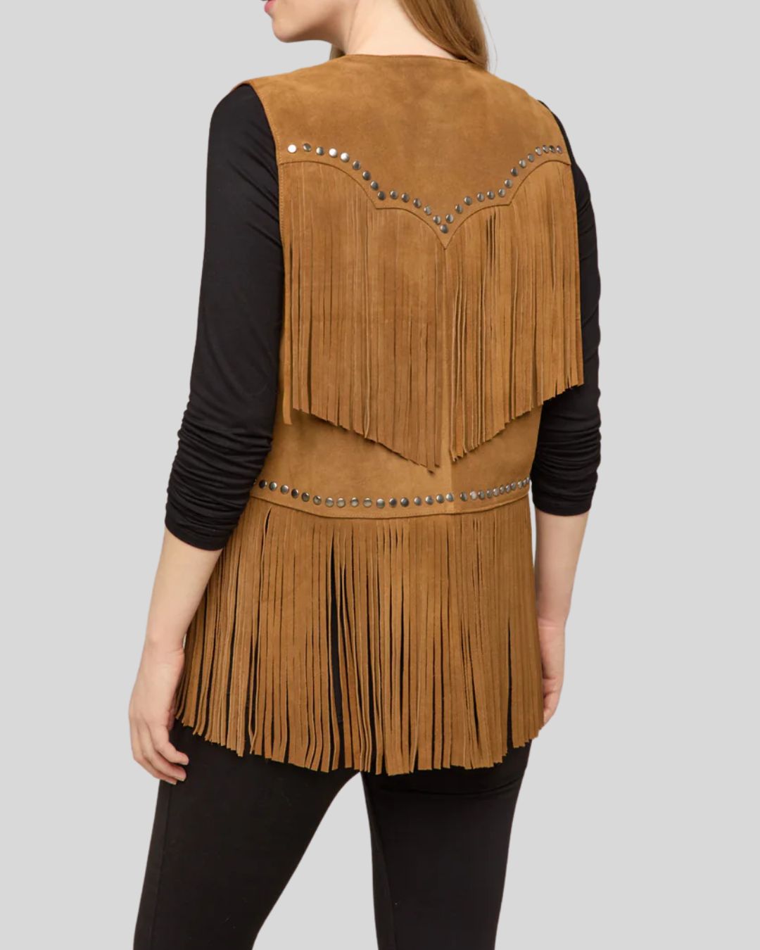 Woman wearing a tan suede fringe vest with studs and western detailing
