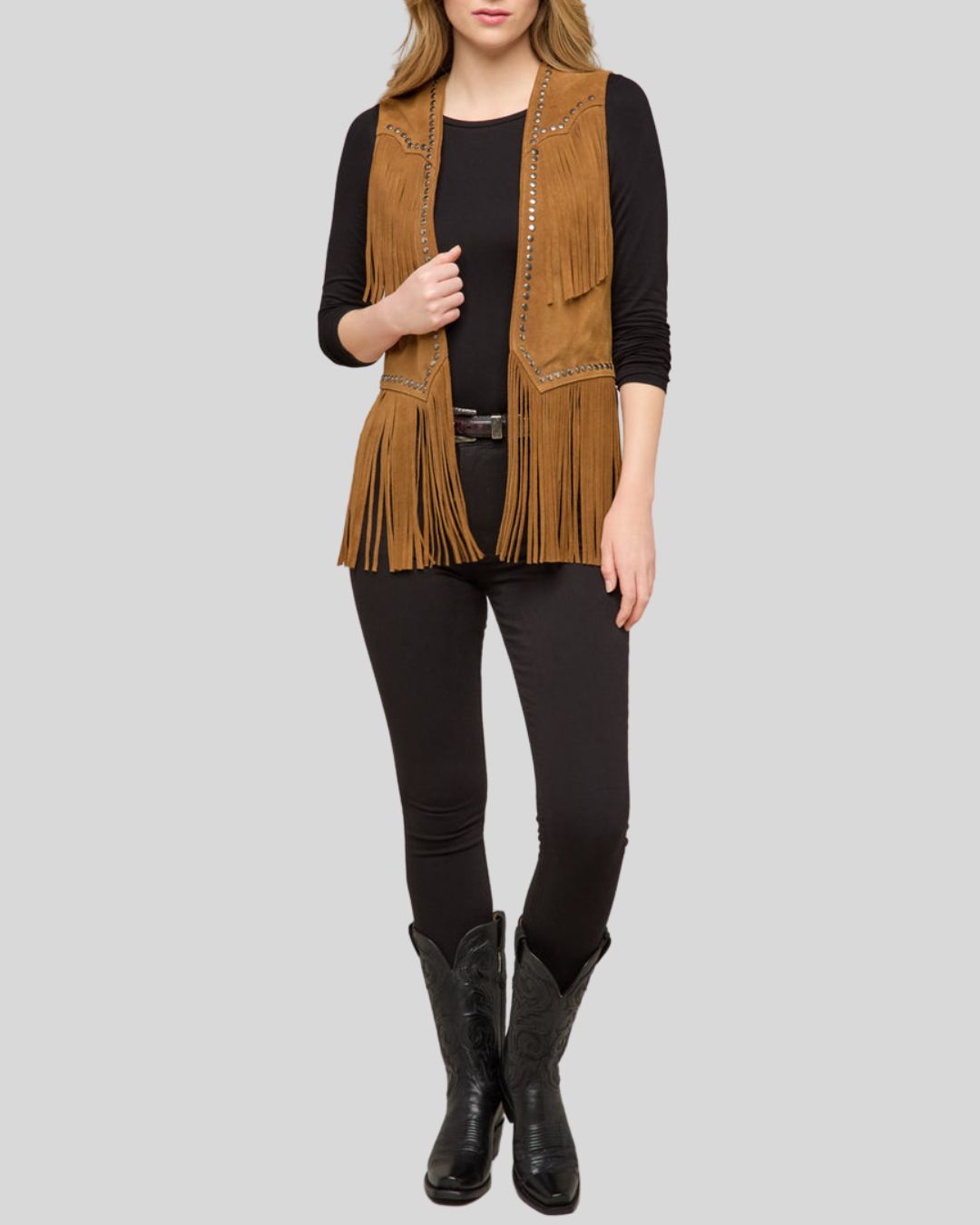 Woman wearing a tan suede fringe vest with studs and western detailing
